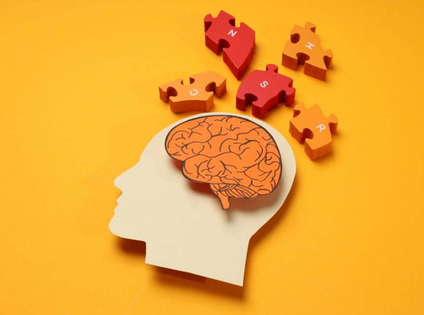 Puzzle of a head with the brain and puzzle pieces on a yellow backdrop.